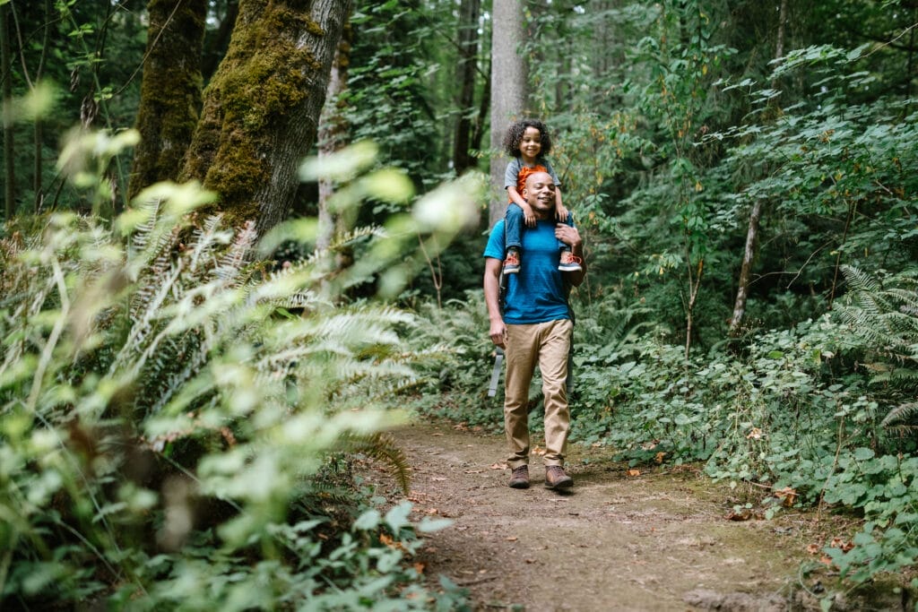 Father Carries Son On Hike Through Forest Trail in Pacific Northwest