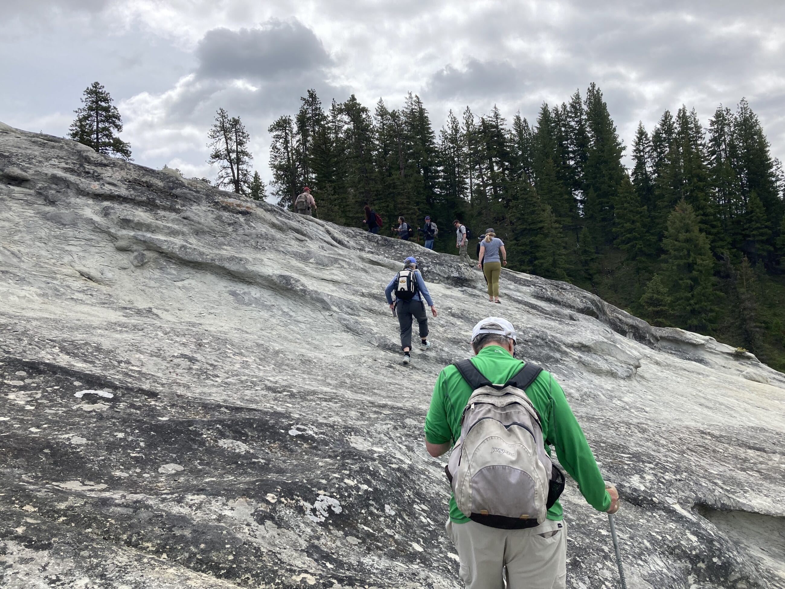 Group of hikers walking up a big slab of gray rock