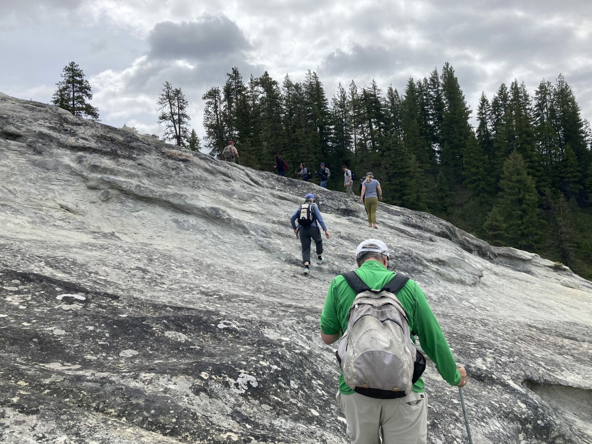 Group of hikers walking up a big slab of gray rock