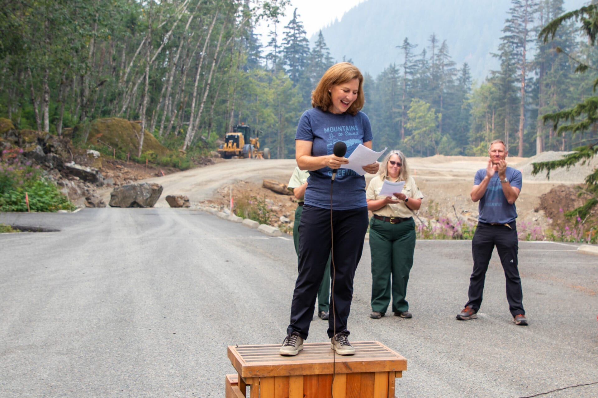 Congresswoman Kim Schrier stands on a podium speaking in front of the Denny Creek construction site
