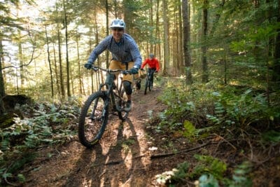 Two bikers ride on a forest trail